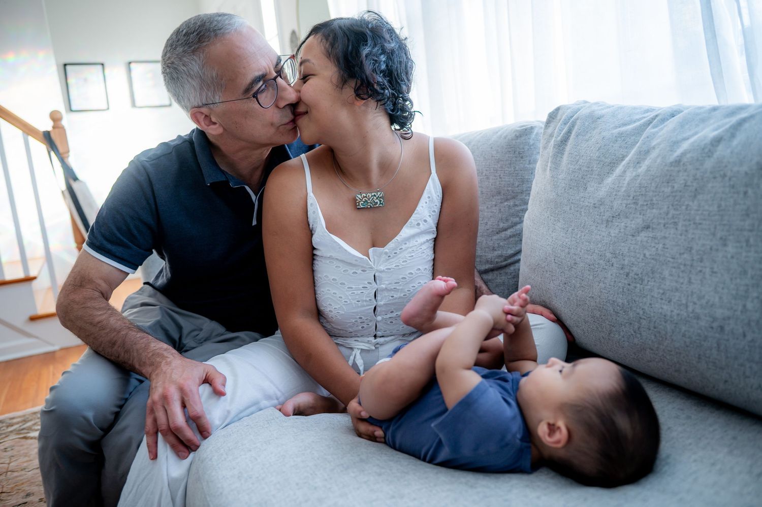 Family members share tender moments while relaxing together on a cozy gray sofa.