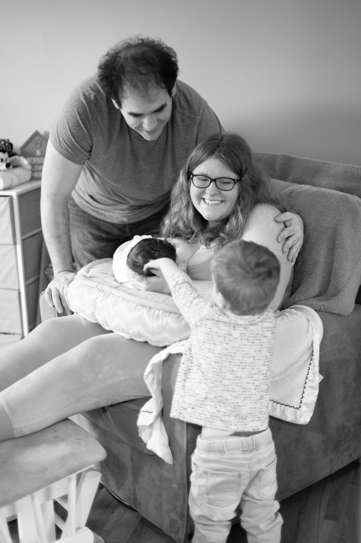 A black and white family moment captured on a couch as they welcome a new baby into their home.