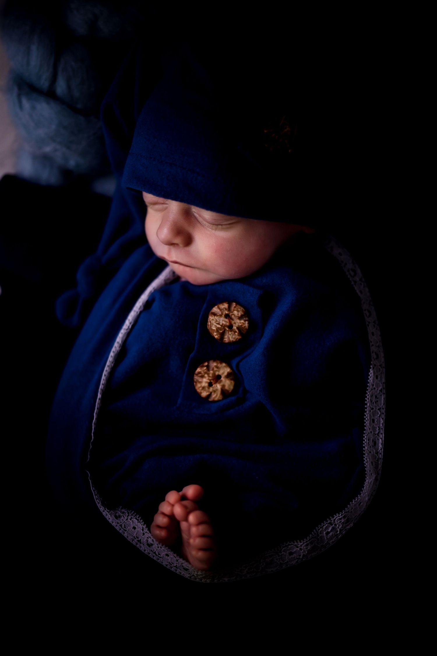 Dark and moody series of a baby in a blue outfit with chocolate chip cookies against a black background.