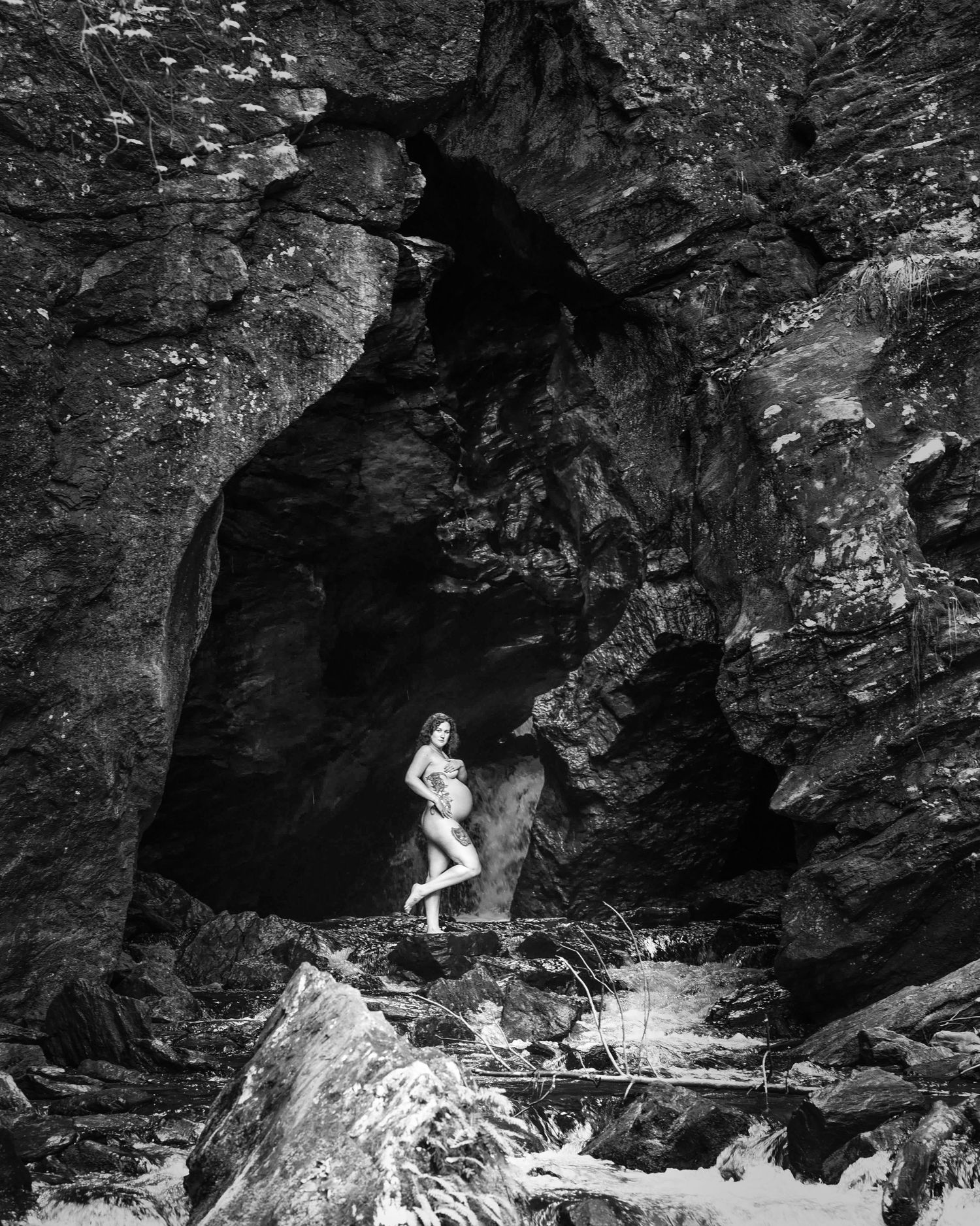 Vintage black and white photograph of a person exploring a rocky cave formation with dramatic shadows and light.