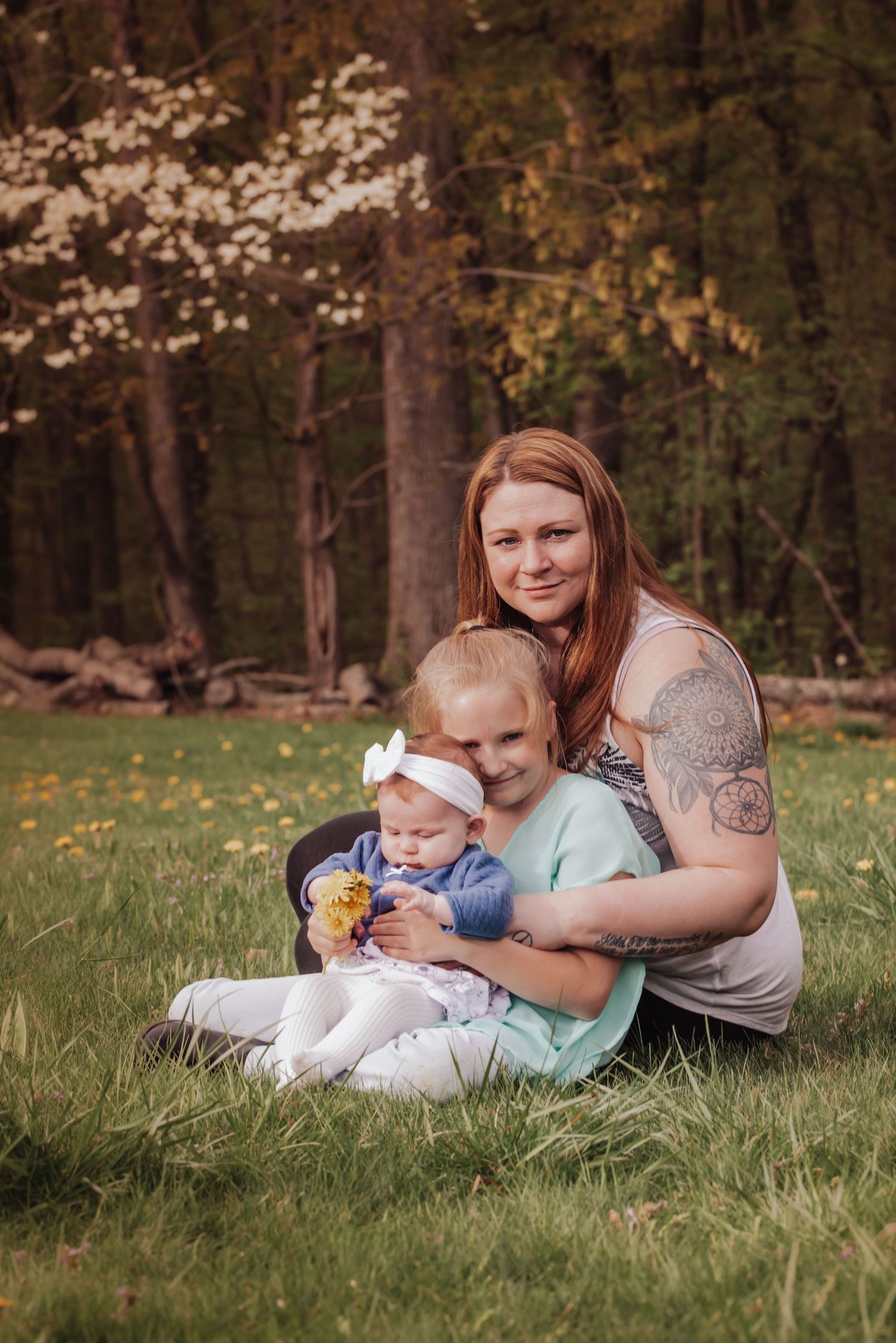 A family sits together on grass in a wooded area during spring with cherry blossoms blooming in the background.