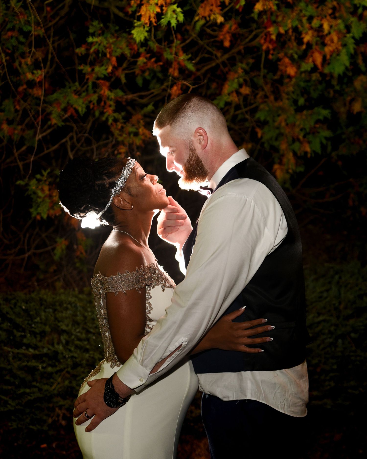 Romantic nighttime wedding portraits with dramatic backlighting among autumn foliage.
