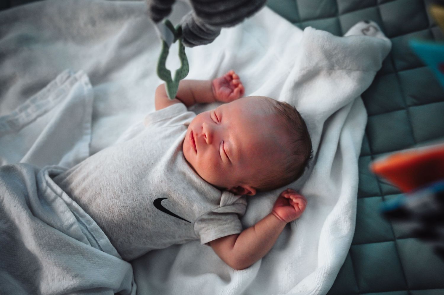 Newborn baby sleeping peacefully on white hospital blanket with medical equipment visible in background.
