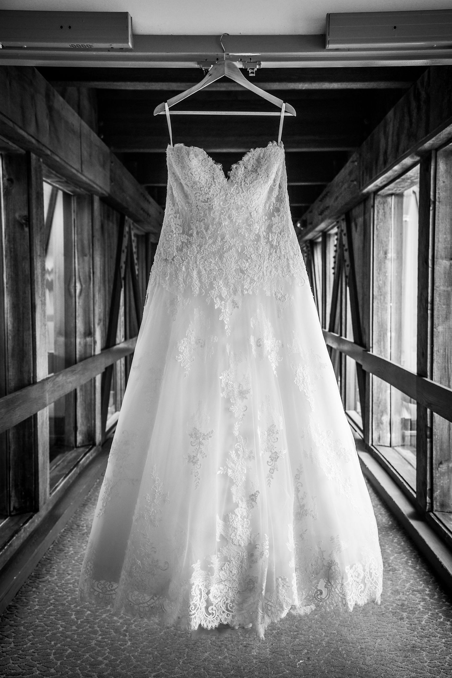 Wedding dress hanging in window corridor showing intricate lace details.