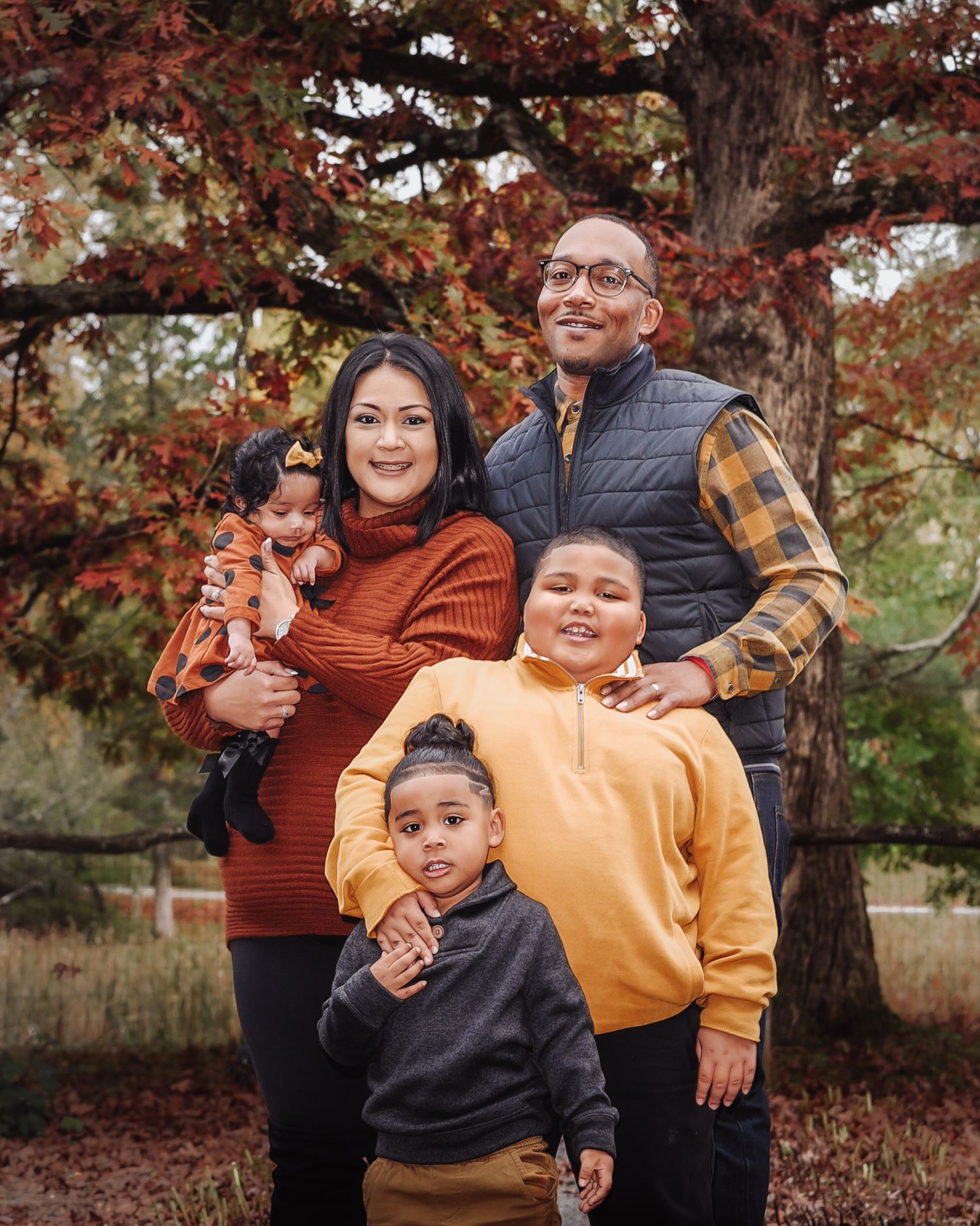 A family enjoys a playful moment together outdoors during autumn with colorful fall foliage in the background.