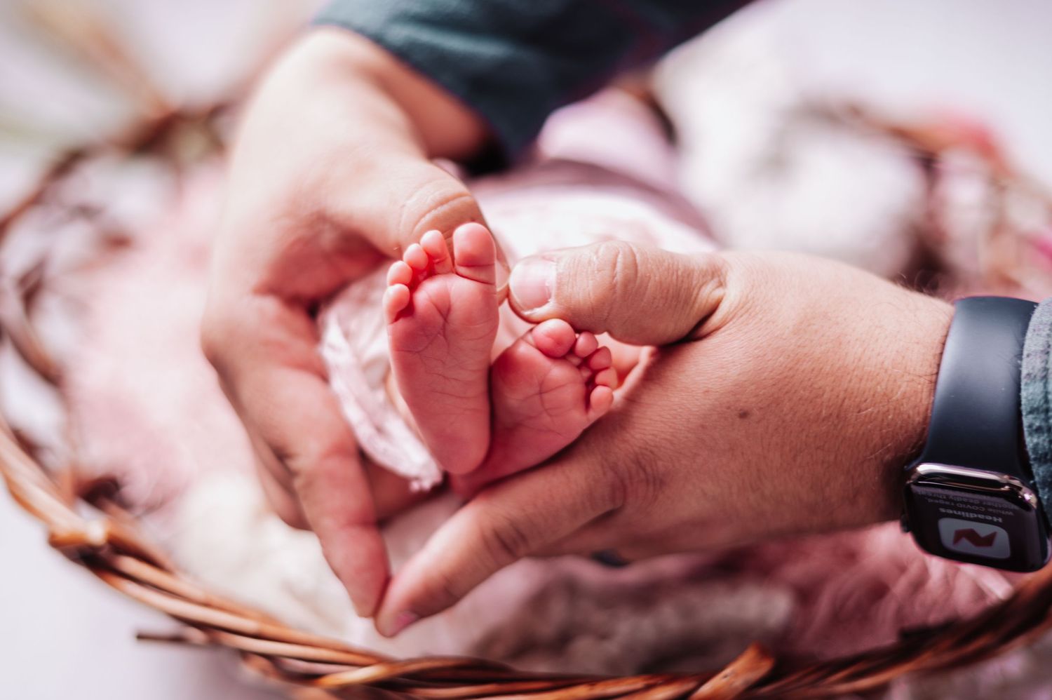 Tiny newborn baby feet cradled gently in adult hands against a soft pink background.