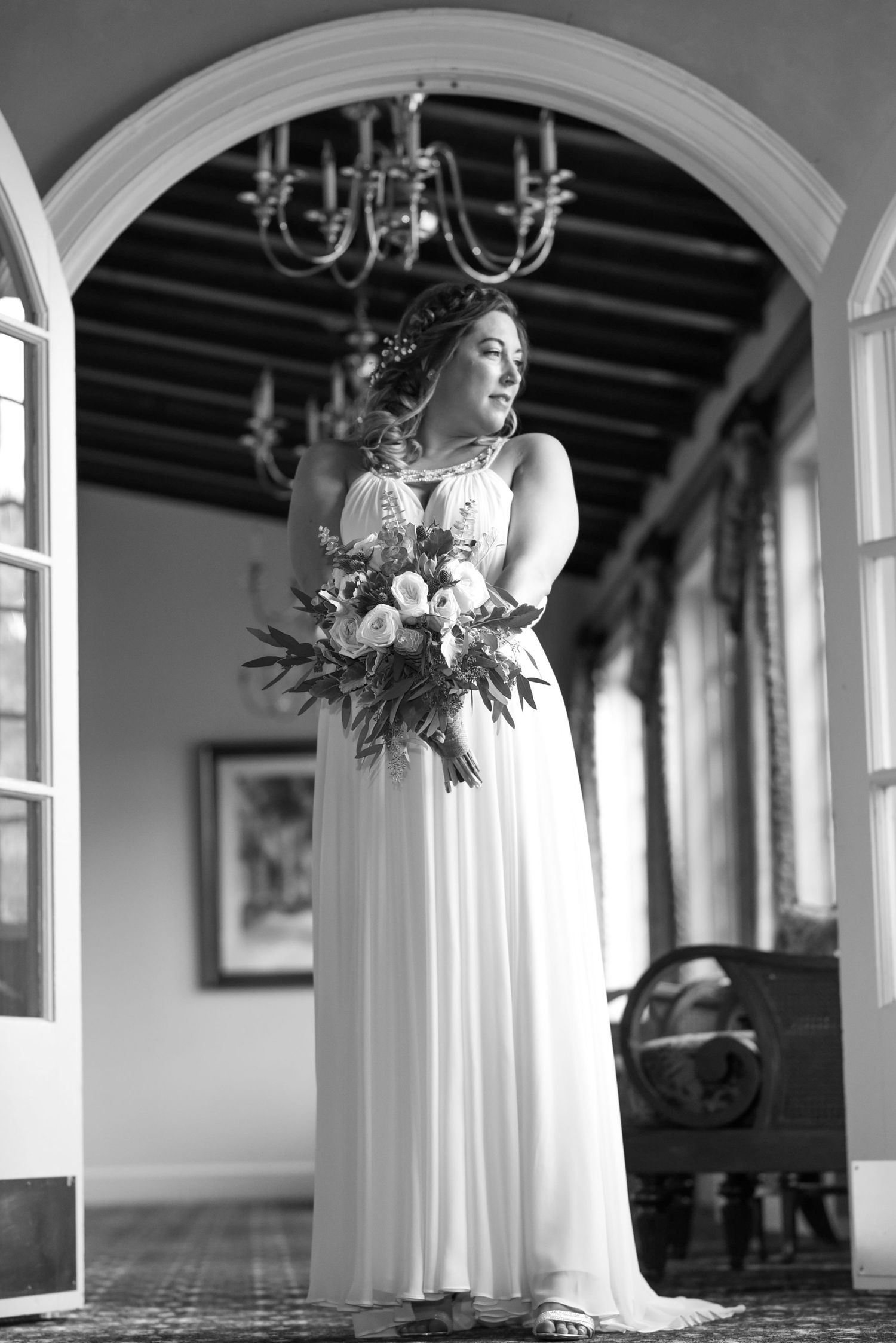 Black and white photograph of a columned hallway with arched architecture and chandelier.