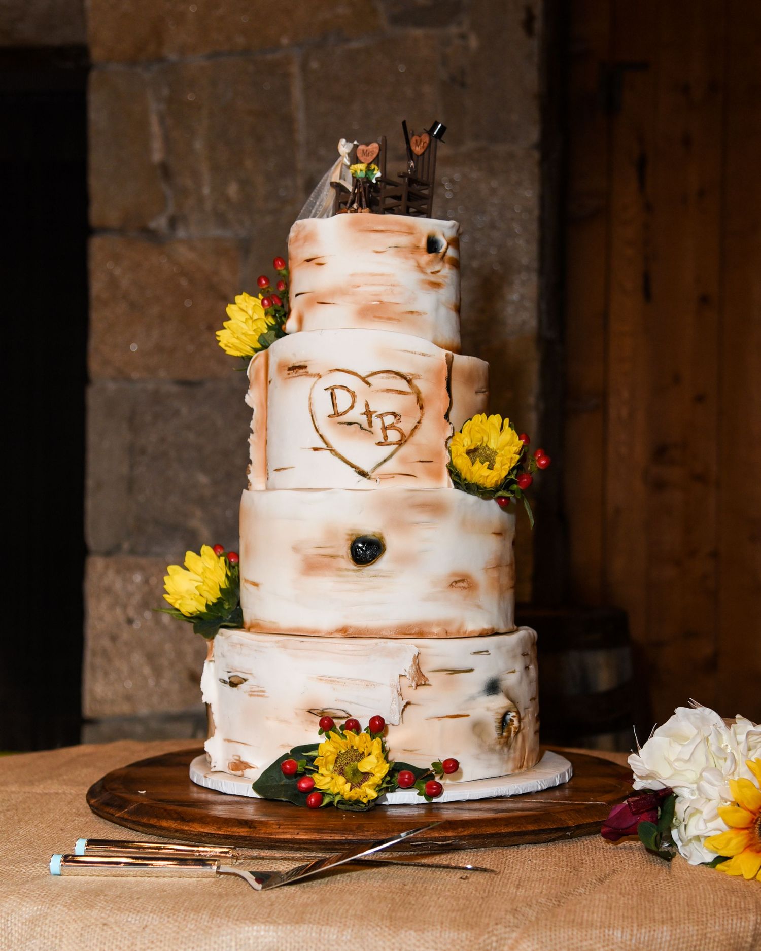 Rustic three-tier birch-themed wedding cake decorated with yellow sunflowers and carved initials.