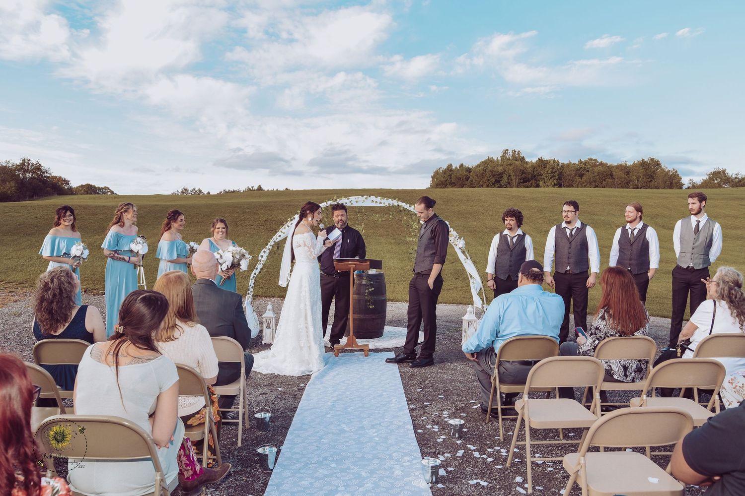 An outdoor wedding ceremony setup with white chairs and aisle runner against a scenic countryside backdrop.