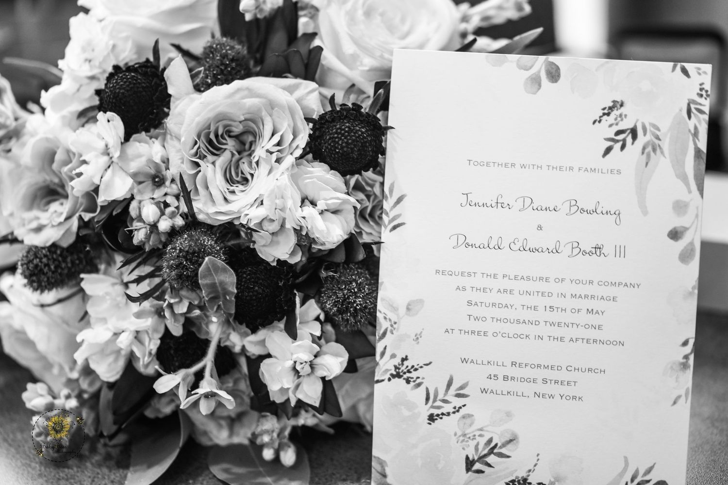 Wedding invitation card displayed next to an elegant floral bouquet with roses and greenery.