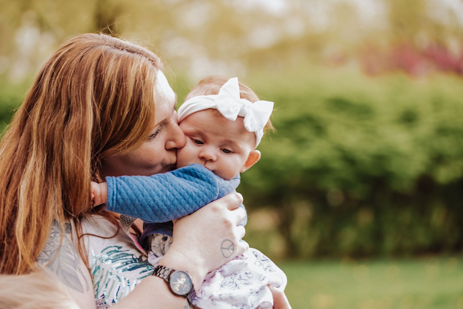 Mother and baby share tender moments in outdoor garden setting with soft natural lighting and blurred background.
