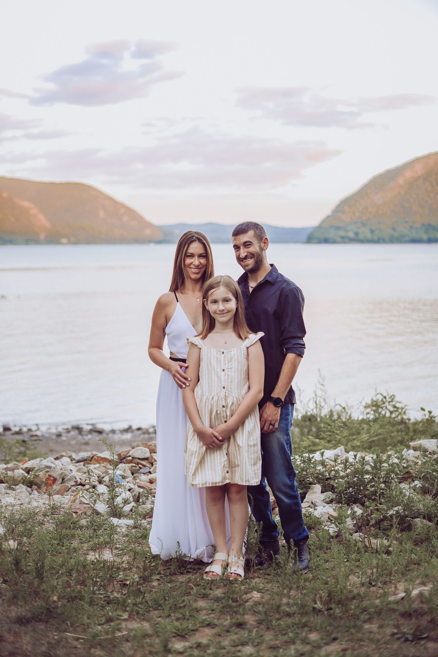 Couple posing together by a scenic lake with mountains in the background during sunset.