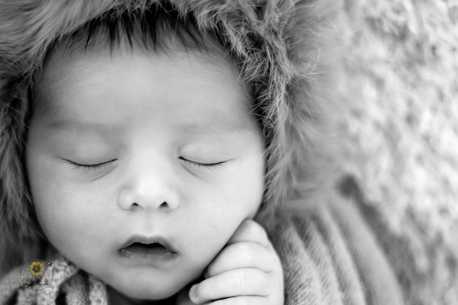 A peaceful sleeping baby in black and white close-up portrait rests against a soft textured blanket.