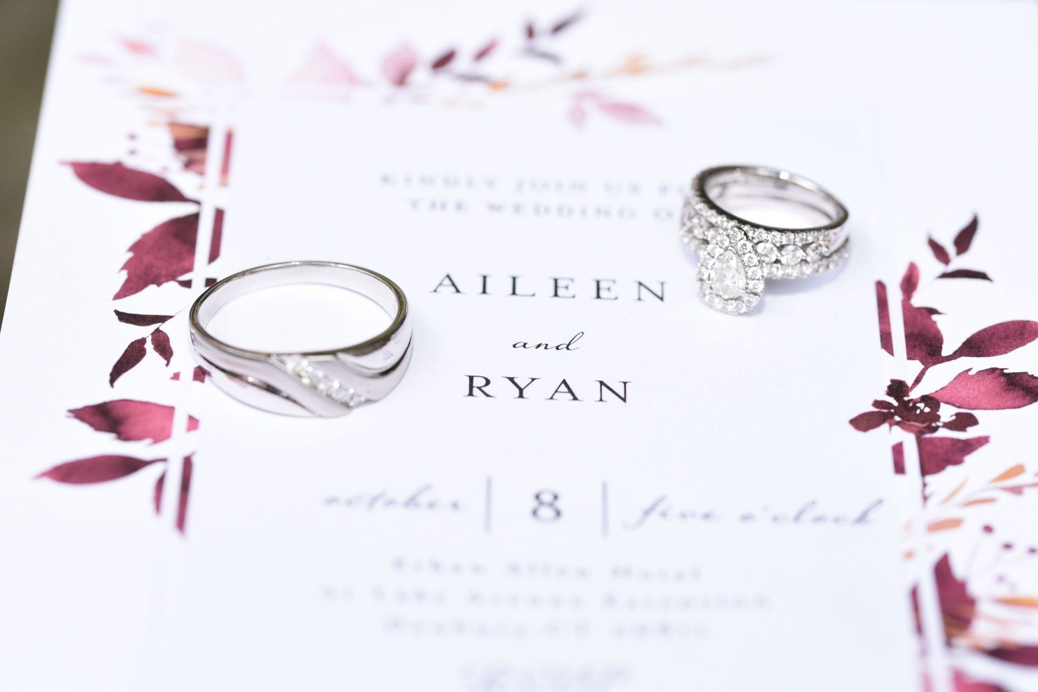 Wedding rings photographed on floral wedding invitation with burgundy watercolor details.