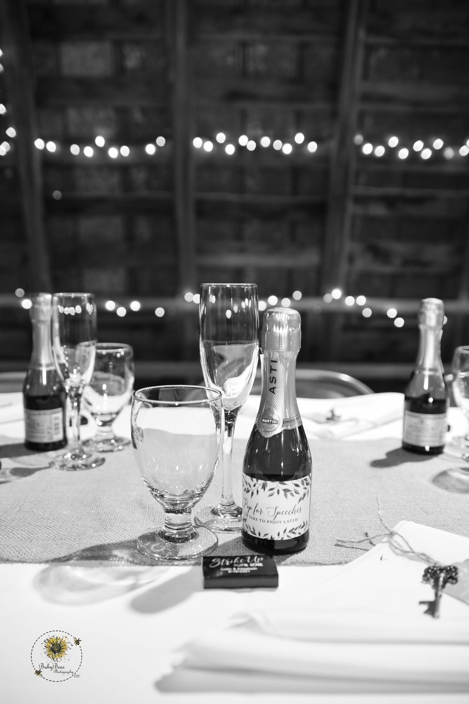 Black and white photo of champagne bottles and glasses set on an elegant wedding reception table.
