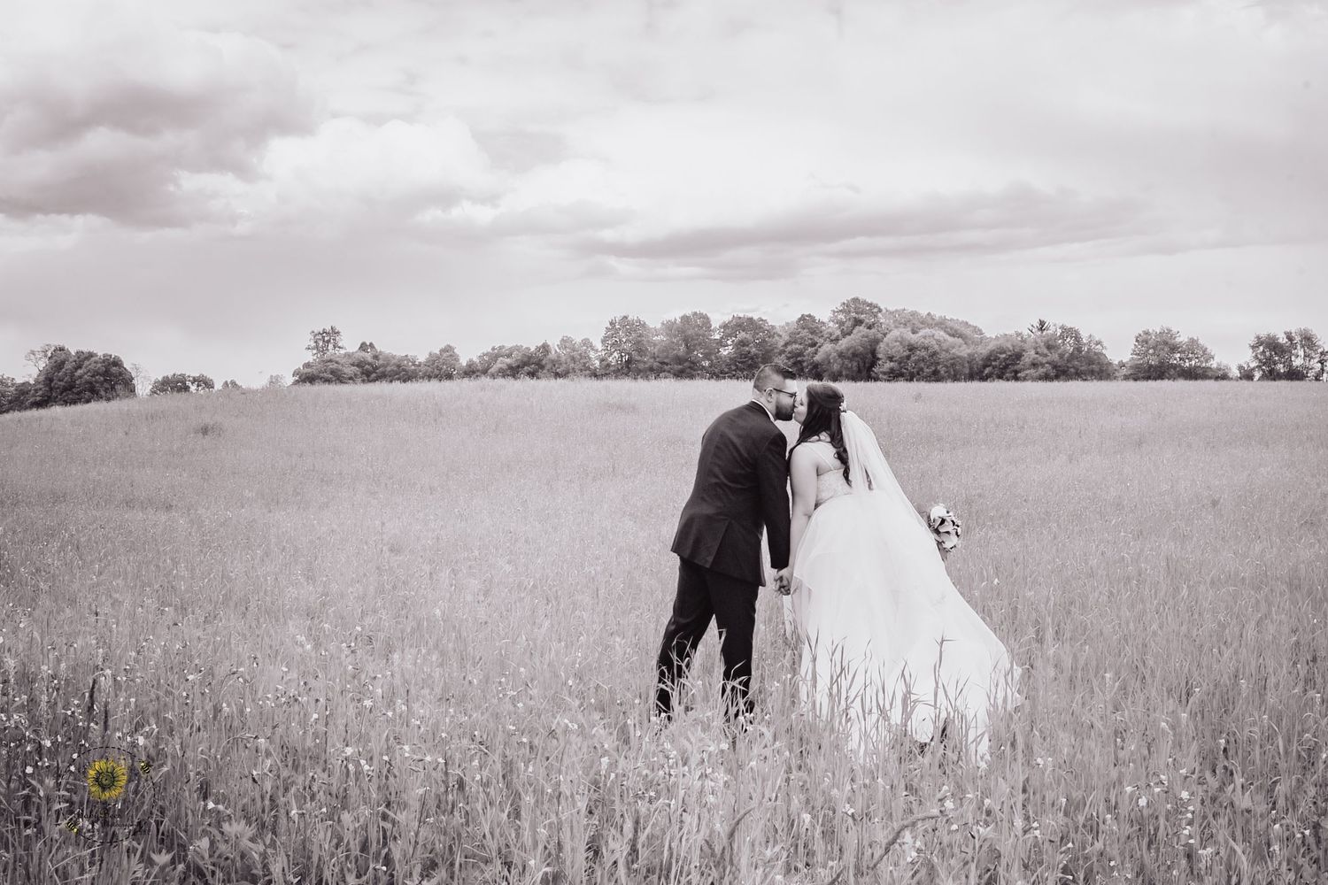 Black and white photo of a wedding couple embracing in a rustic field.