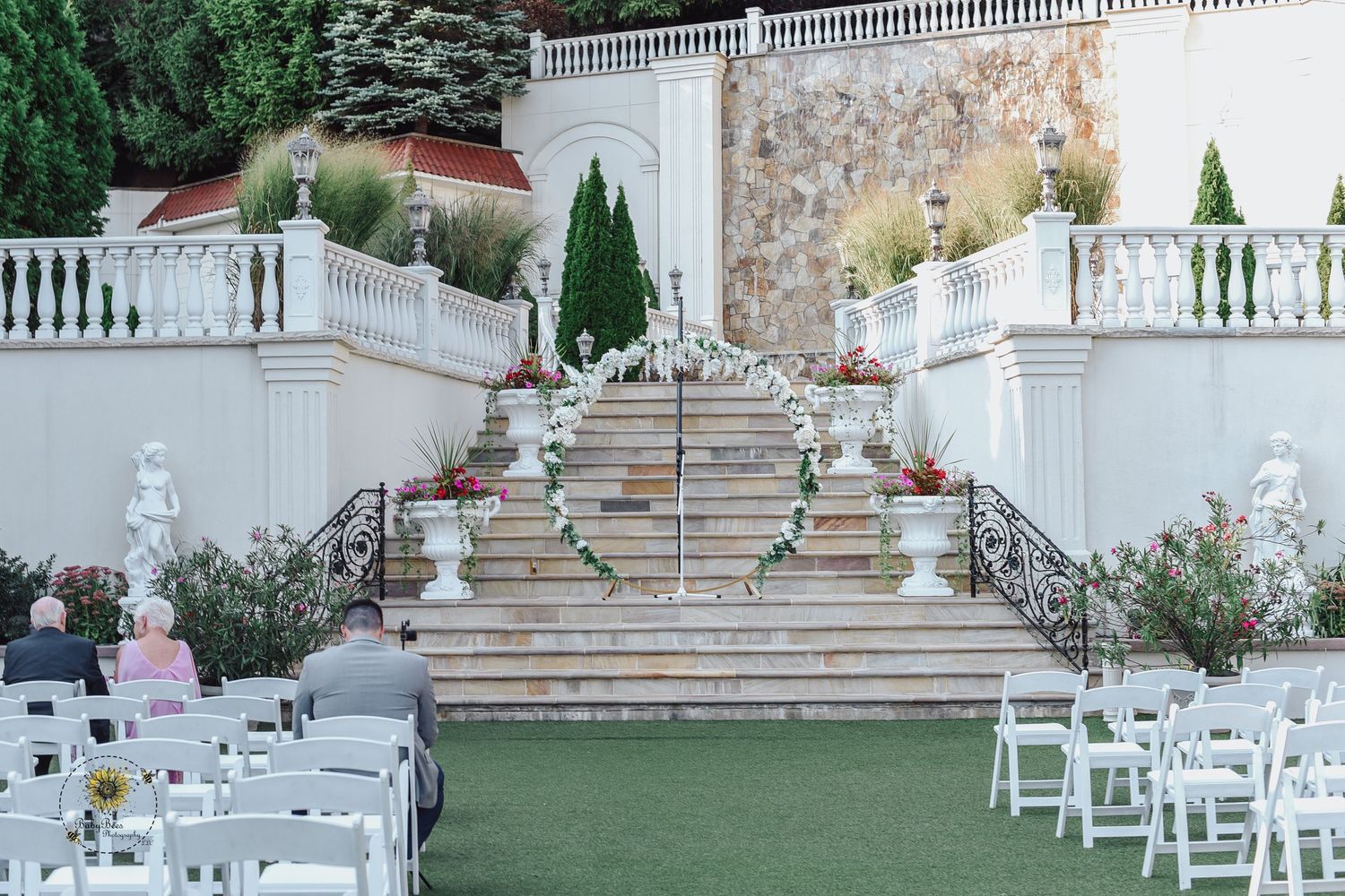 Elegant outdoor wedding venue with white chairs and stone staircase surrounded by lush gardens.