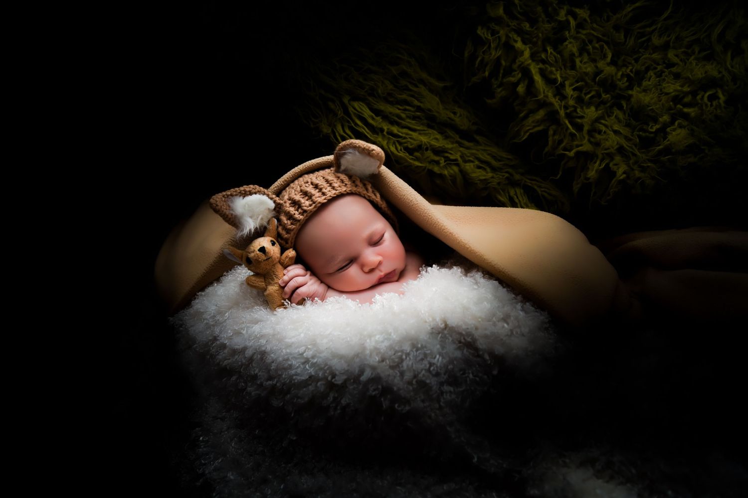 A sleeping newborn baby rests peacefully on soft white fur in dramatic lighting.