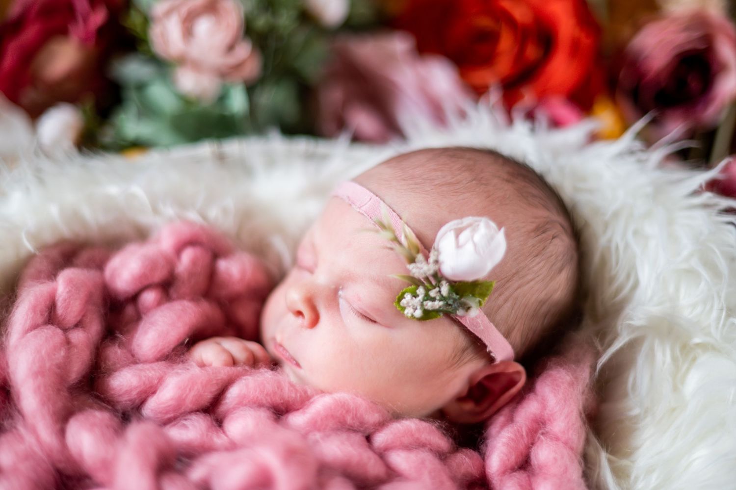 Newborn baby sleeping peacefully on pink blanket with delicate floral headpiece.