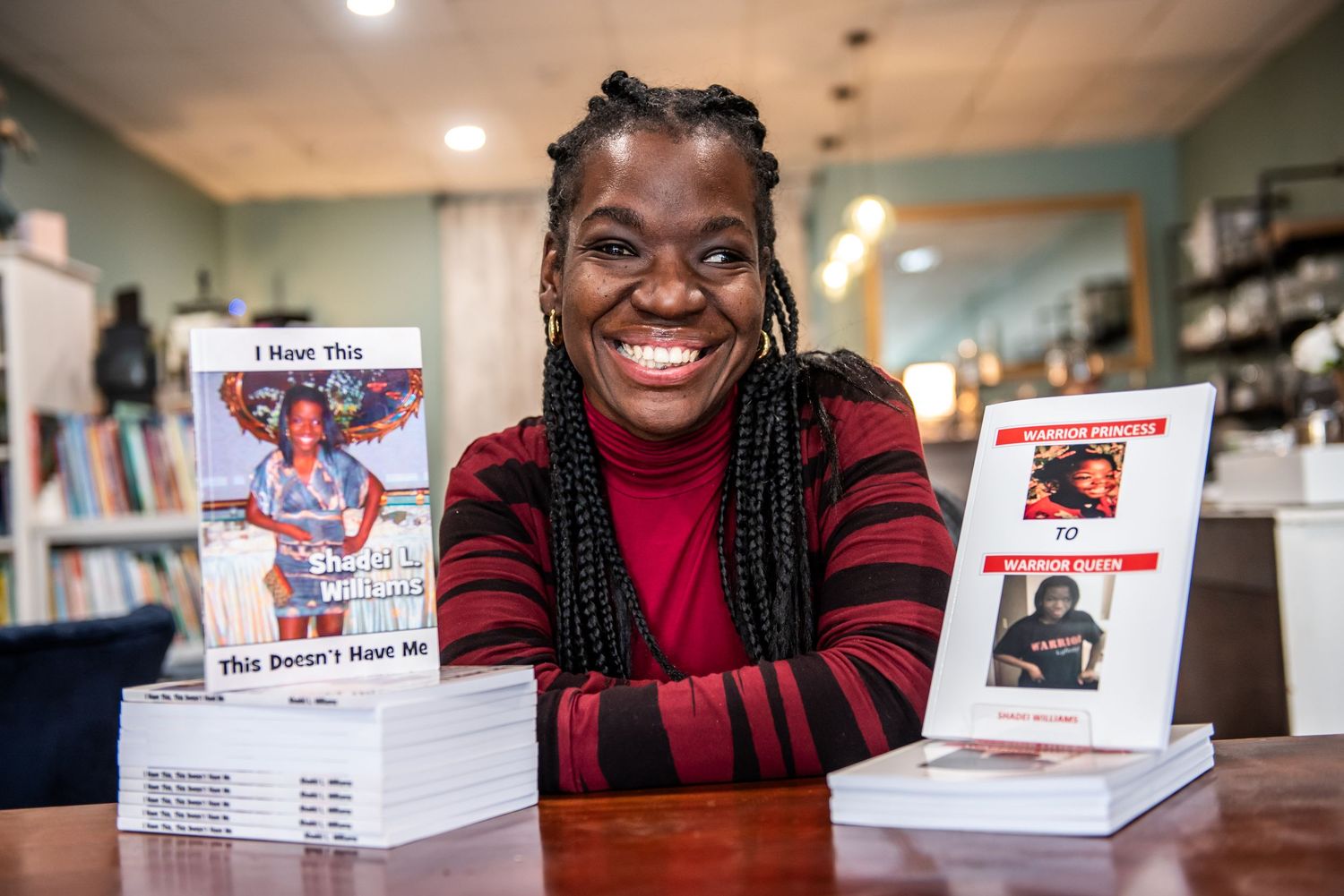 Author sits at table with stacks of books in a bookstore wearing red and black striped sweater.