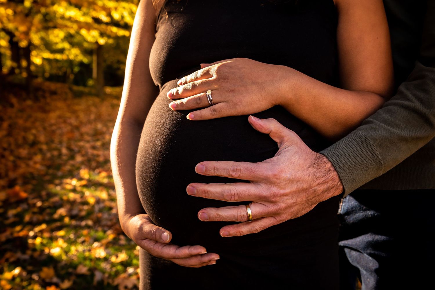 Close-up maternity photo series showing hands cradling a pregnant belly in golden autumn sunlight.