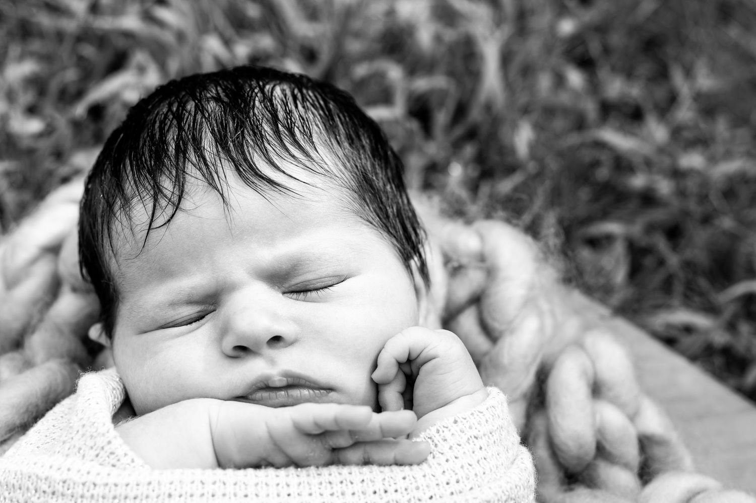 Black and white close-up photo of a sleeping baby with dark hair resting on soft white fabric.