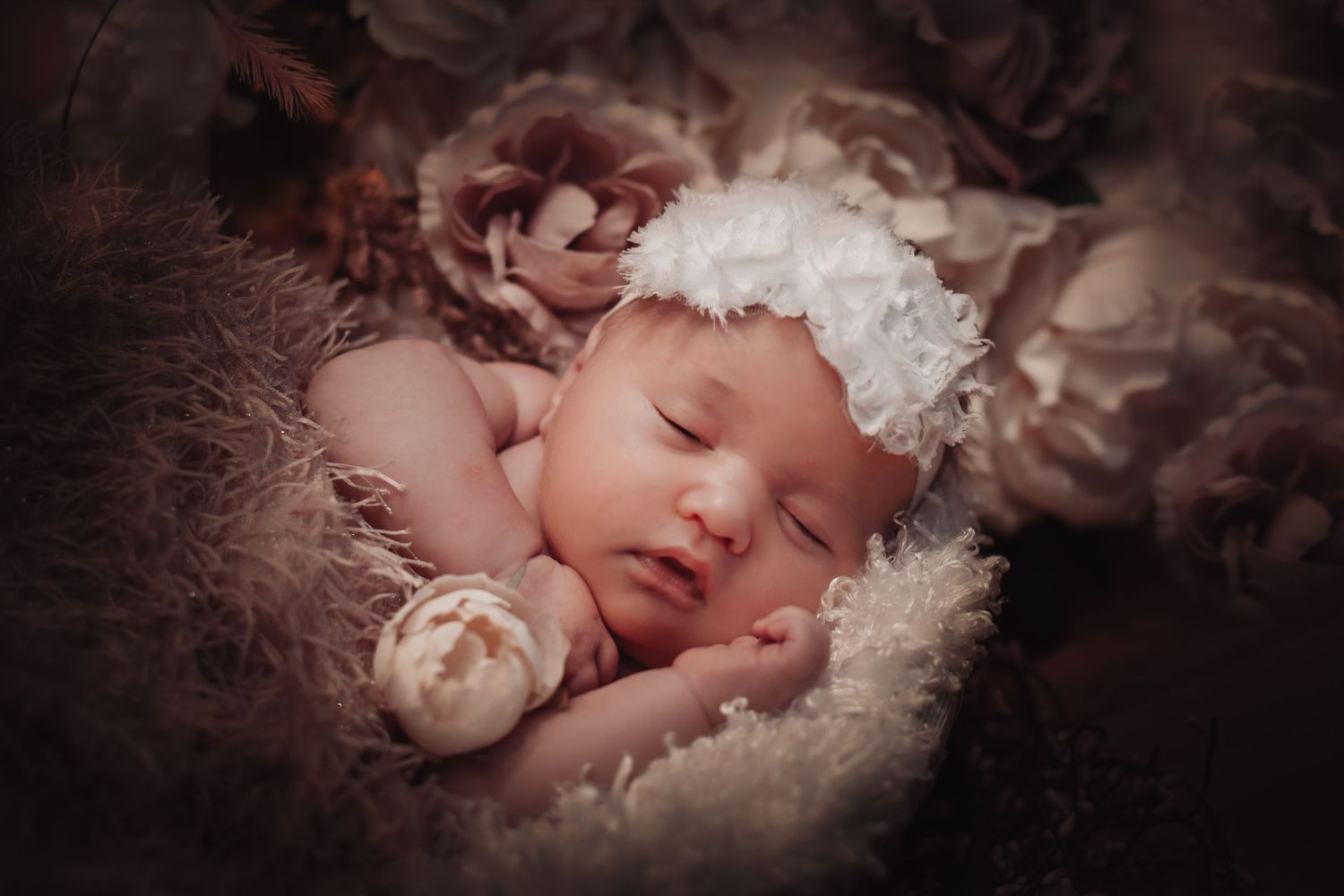 A sleeping newborn baby nestled in soft white blankets with delicate floral decorations surrounding them.