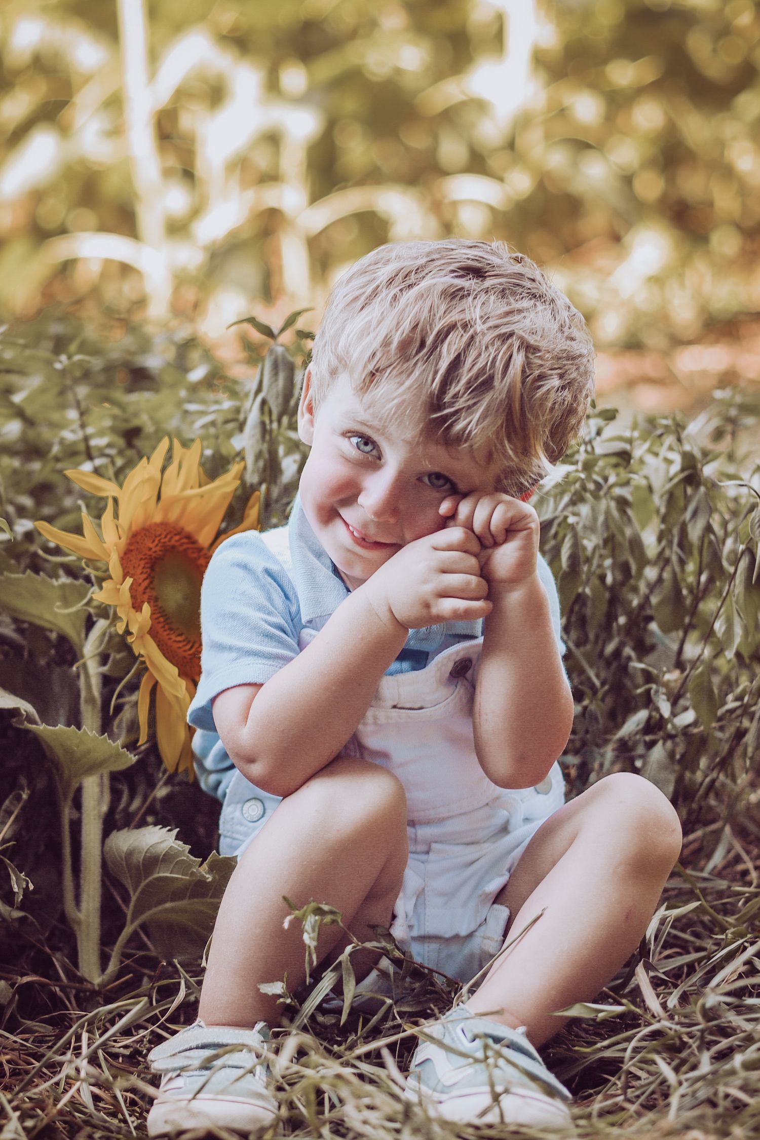A young child sits playfully in a garden of sunflowers on a sunny summer day.