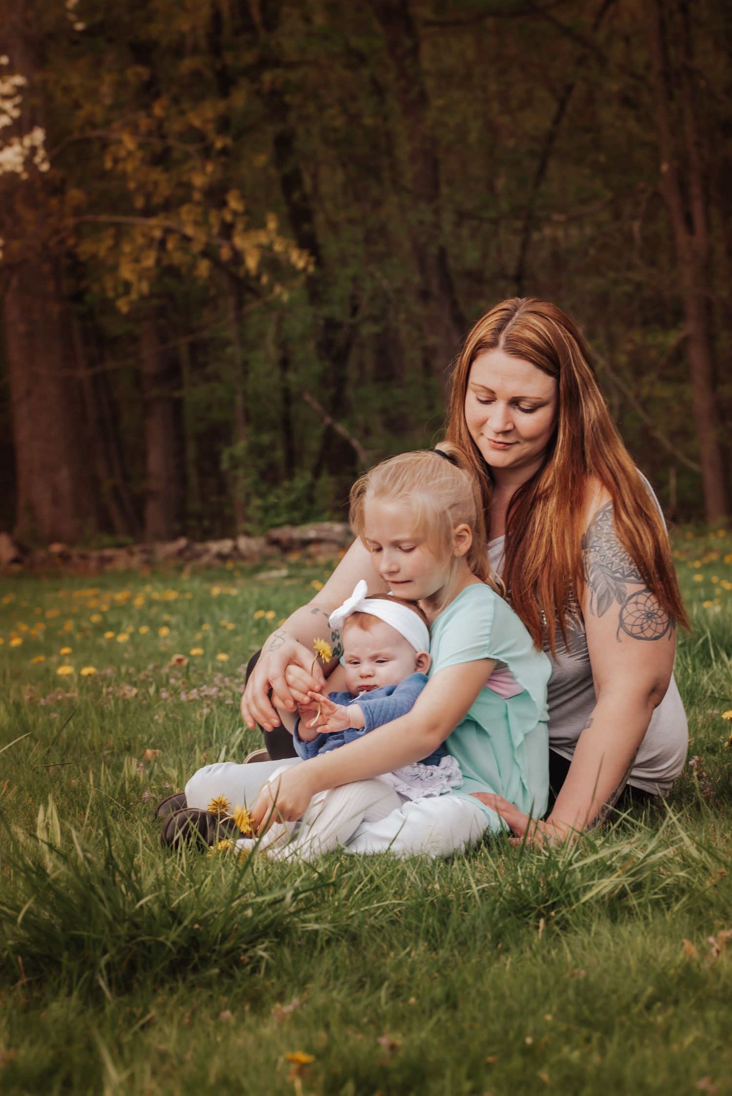 A tender family moment captured in a grassy field with dandelions during golden hour.