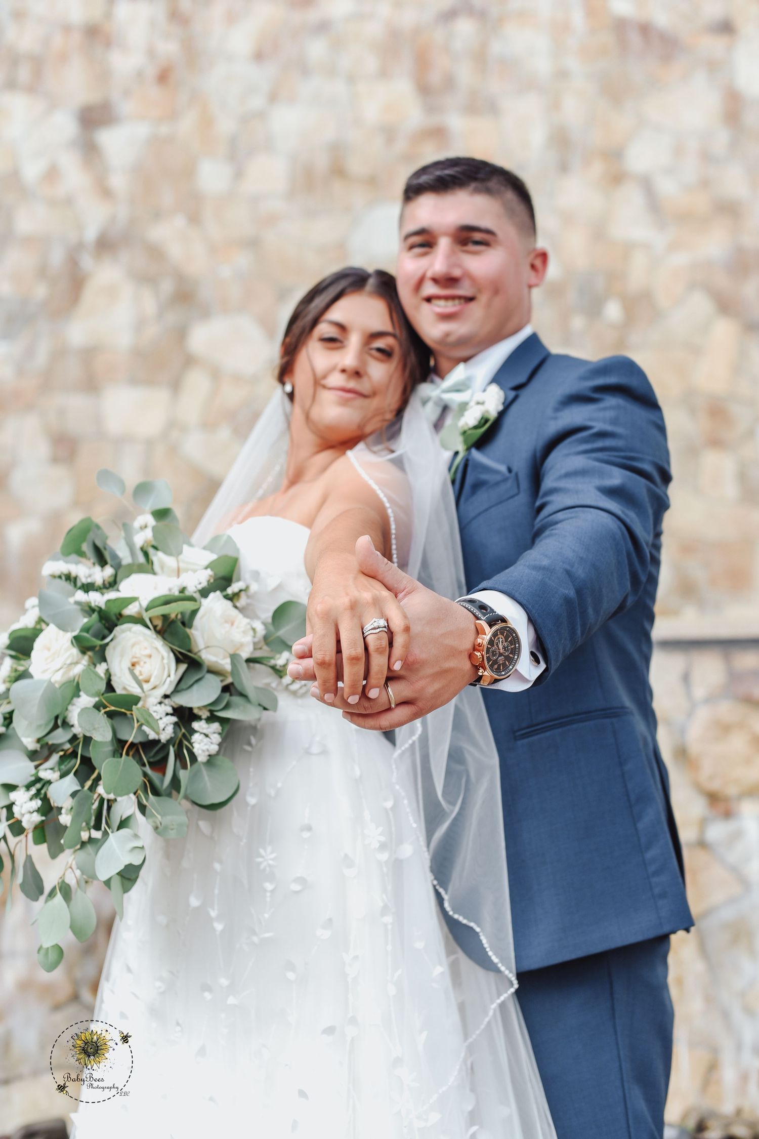 Couple showing off wedding rings with white floral bouquet and eucalyptus.