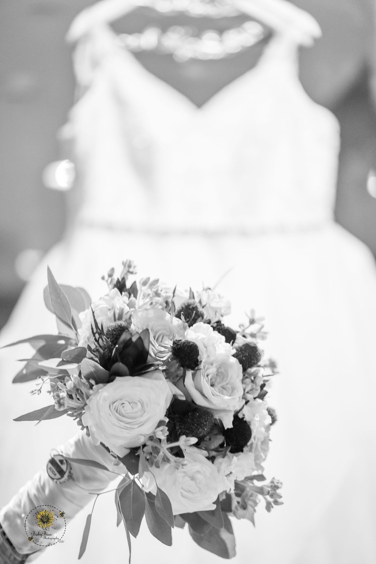 Elegant white wedding dress hangs above a romantic bouquet of roses and mixed flowers in black and white.