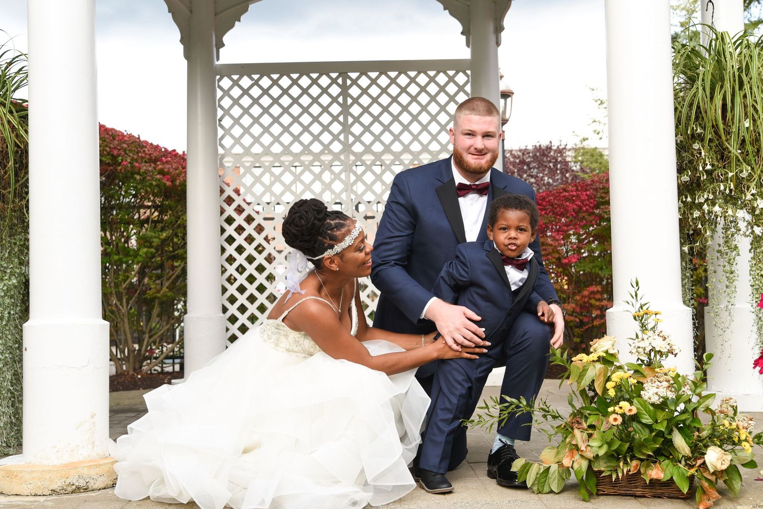 Wedding couple poses under a white pergola in a garden setting.