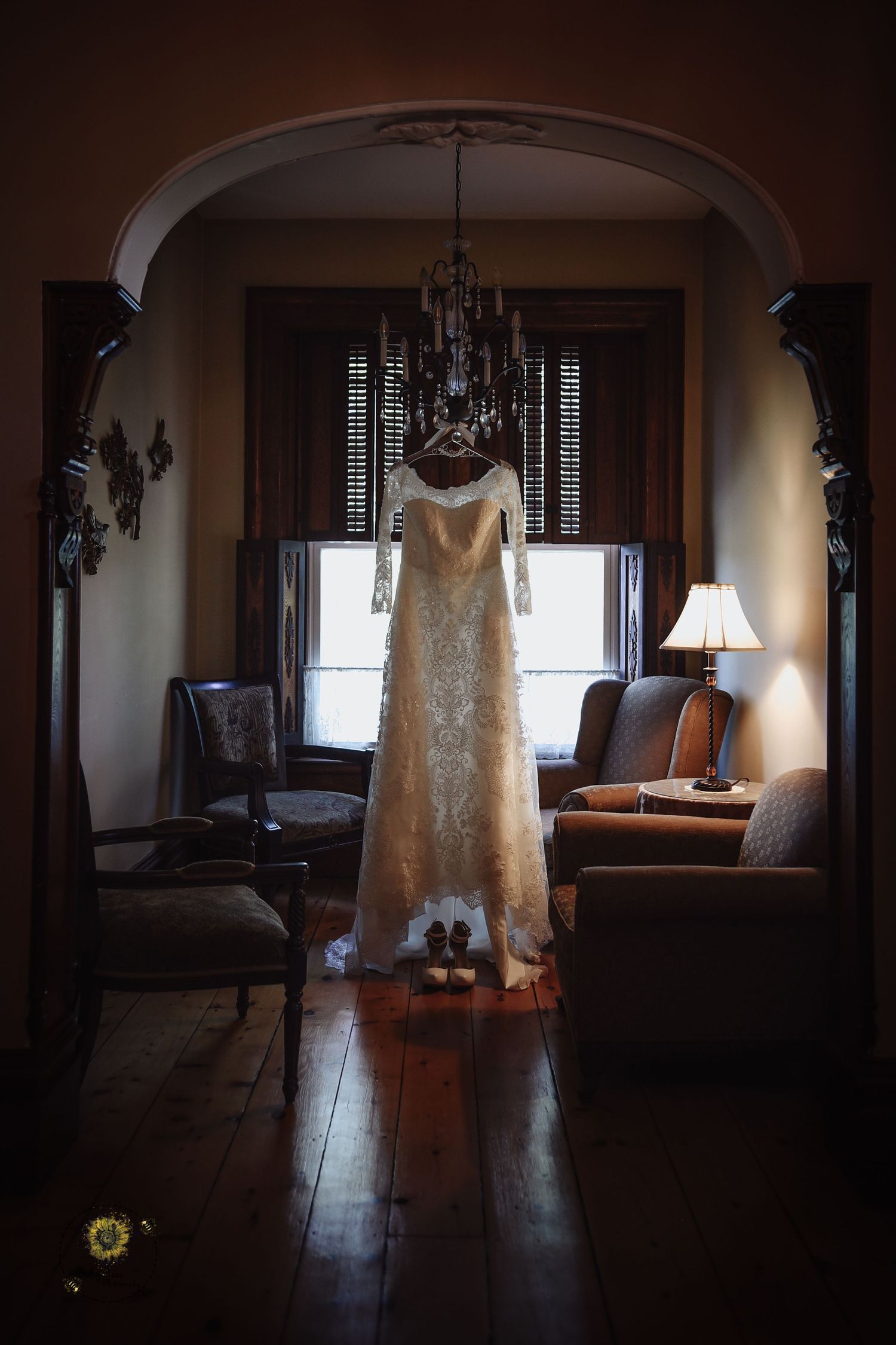 Backlit wedding dress hanging in window creating dramatic silhouette in vintage interior.