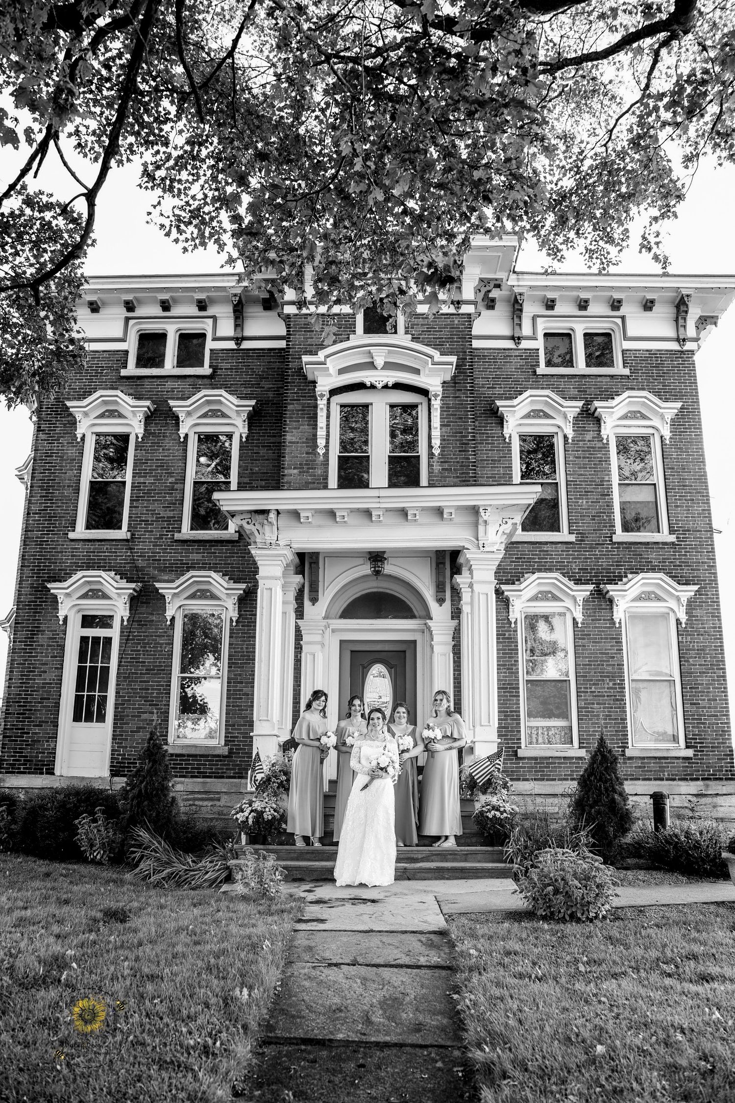 Classic black and white photo of wedding party in front of a grand Victorian brick mansion.