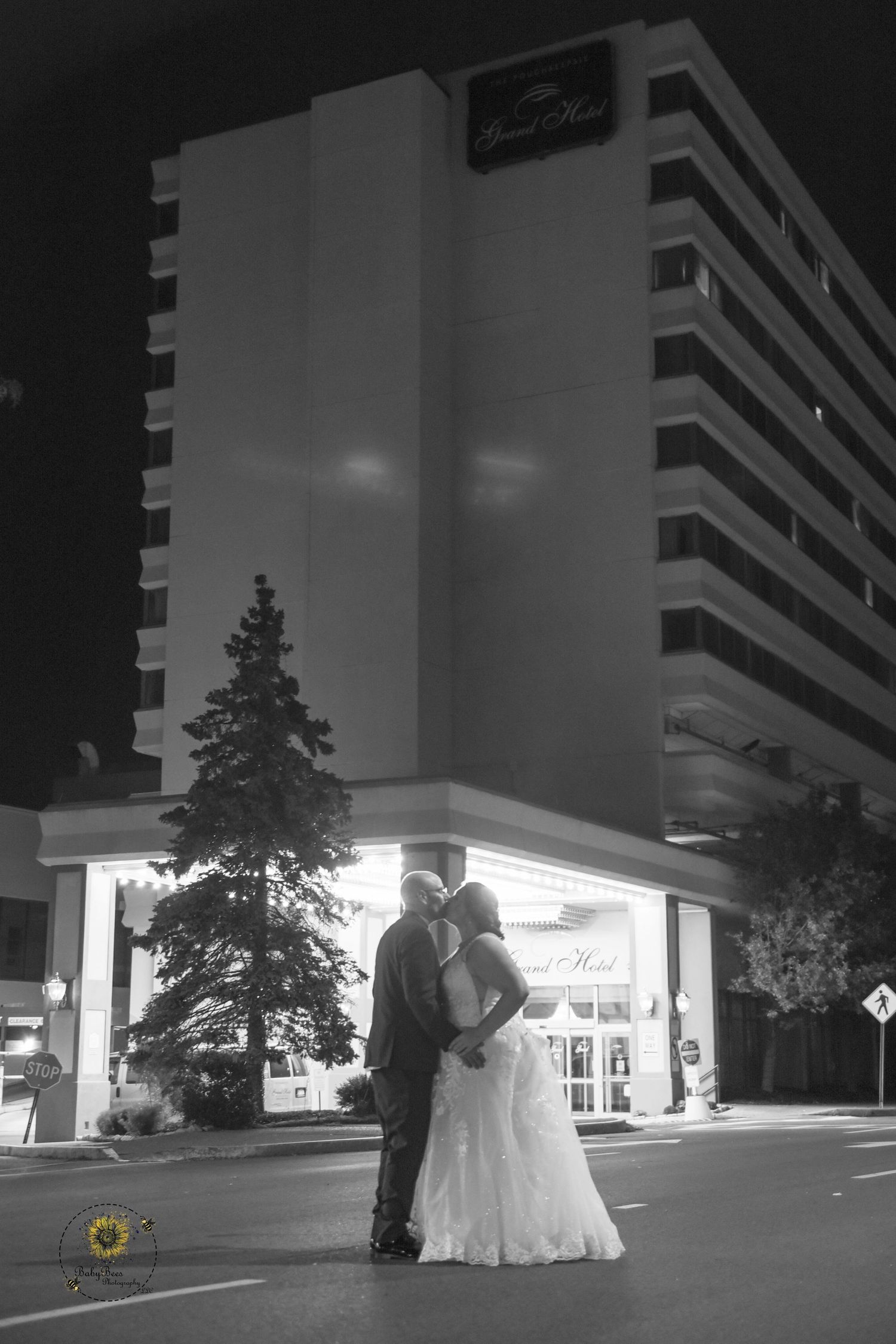 Black and white nighttime wedding photo in front of an illuminated hotel entrance.