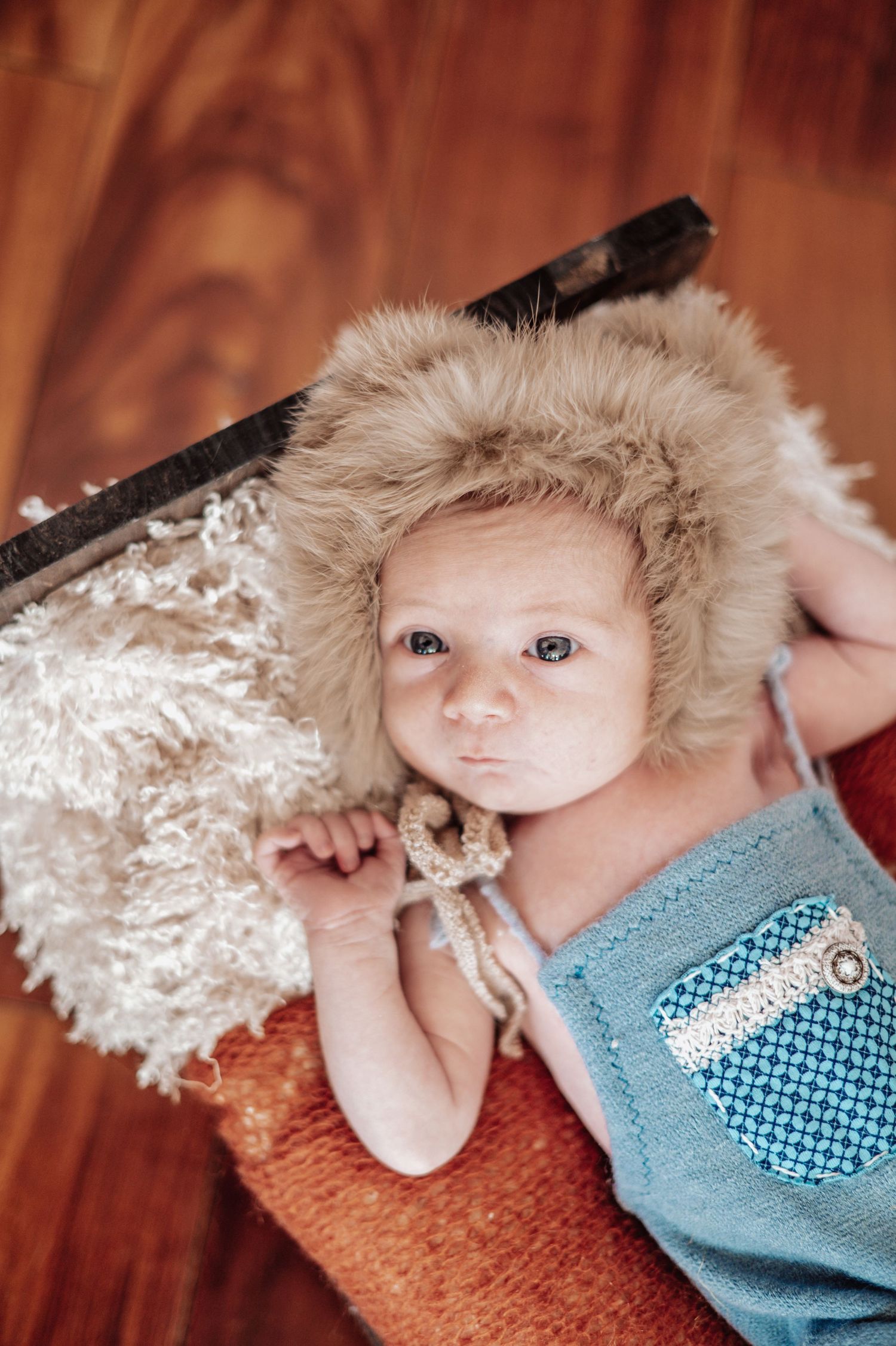 Baby wearing blue outfit lies in brown basket with white decorative material while being photographed from different angles.