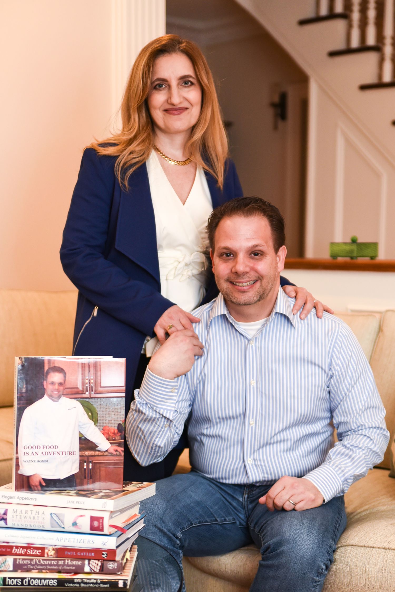 Two people sit together on a couch reviewing documents and books in a home setting.