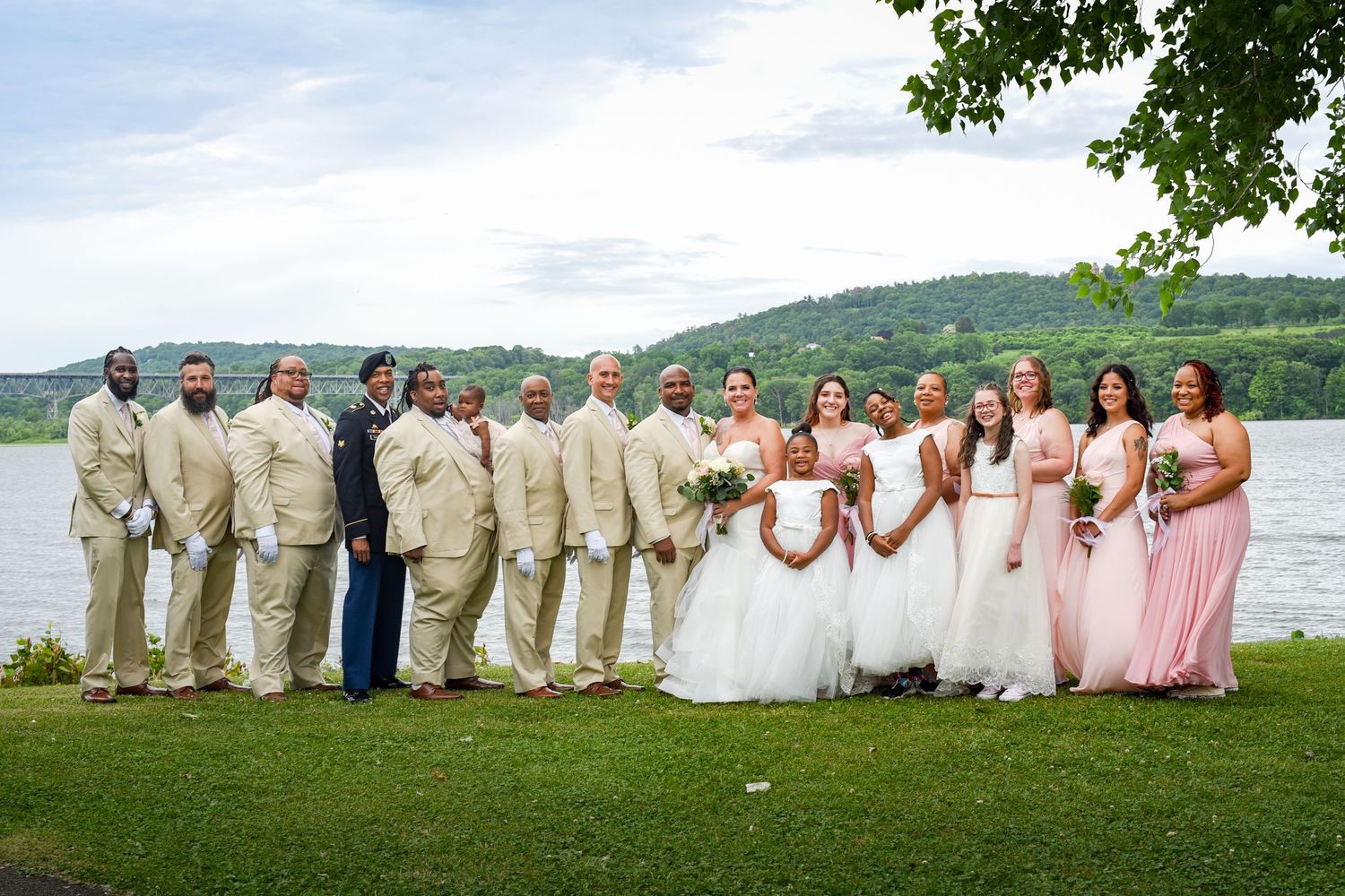 Wedding party in cream colored attire poses by a scenic lake with mountains in background.