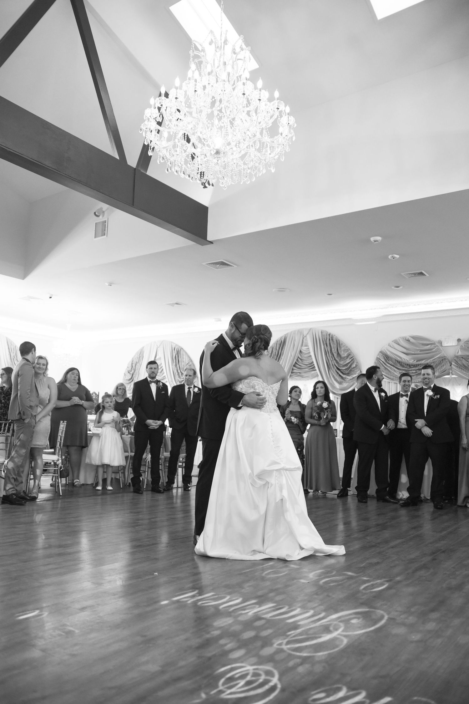 A couple shares their first dance under an elegant crystal chandelier at their wedding reception.