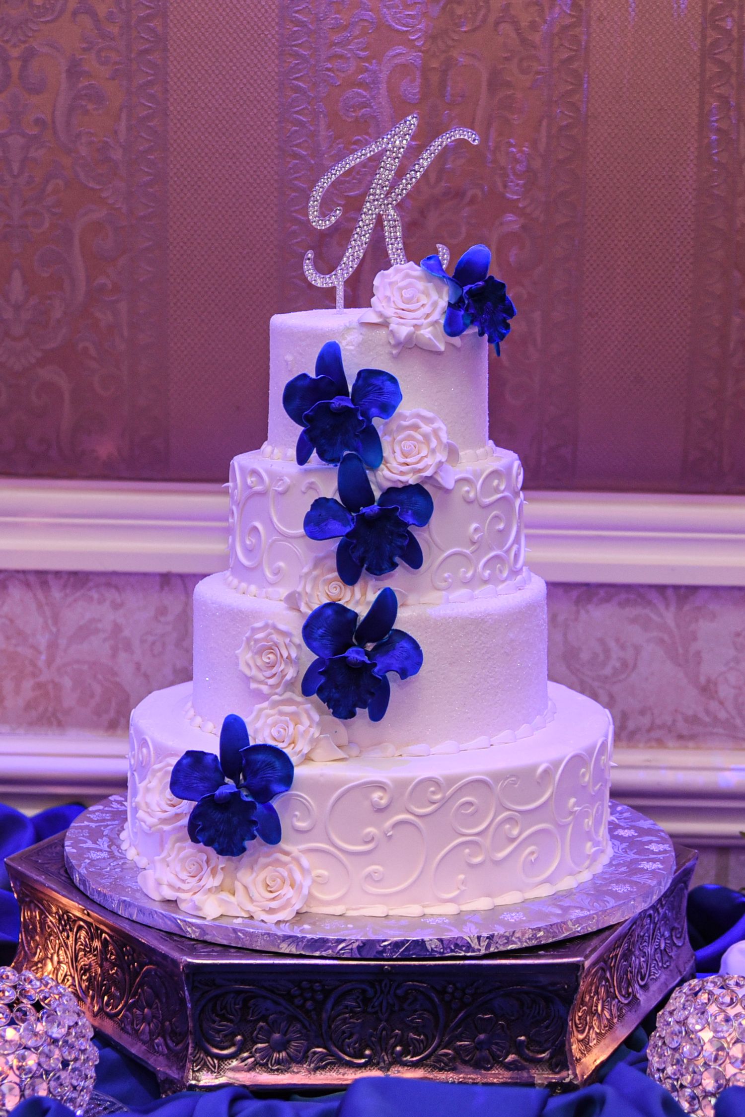 Elegant white wedding cake decorated with royal blue orchids and intricate piping details.