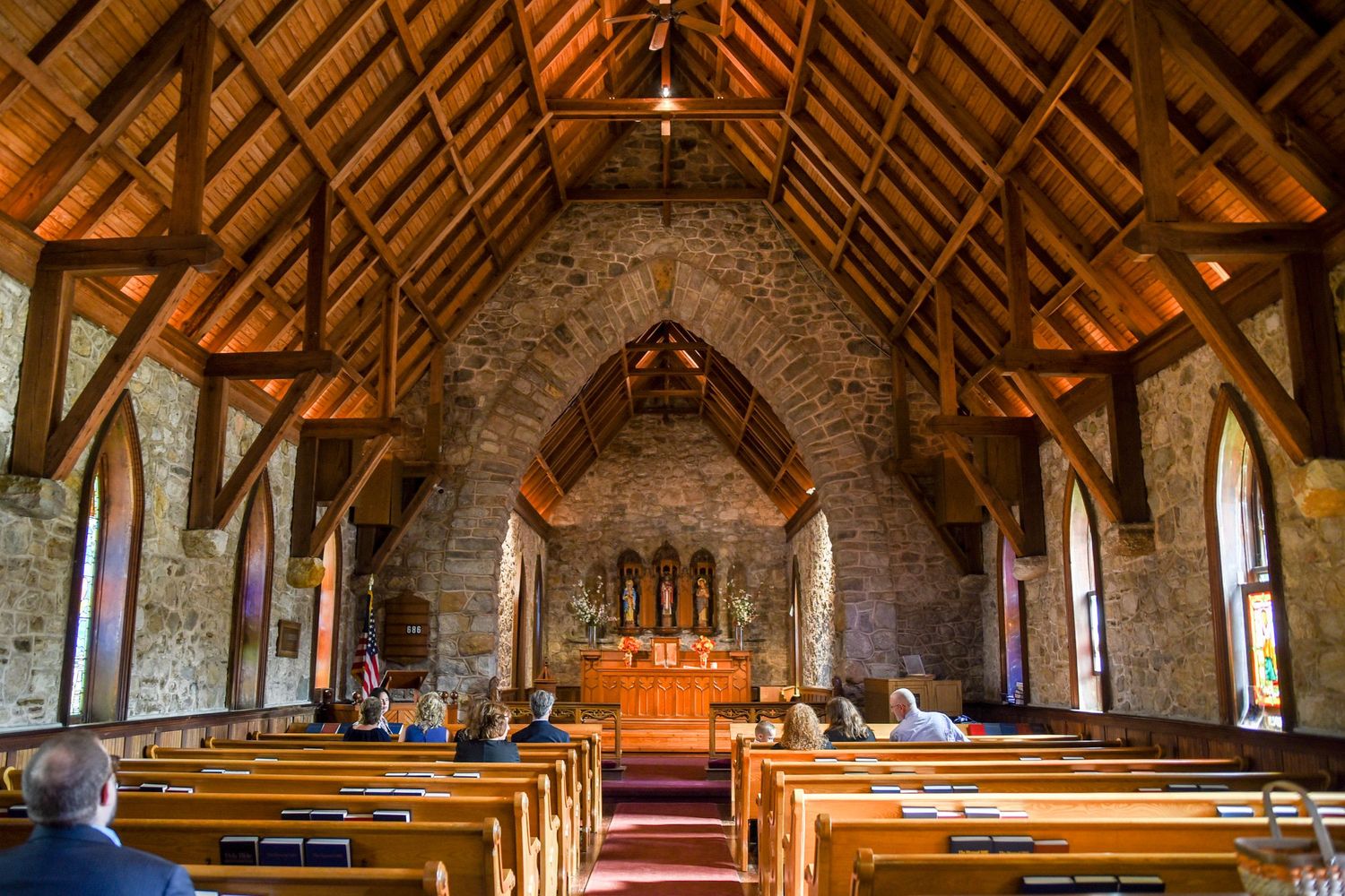 Rustic stone church interior with exposed wooden beams and vaulted ceiling.