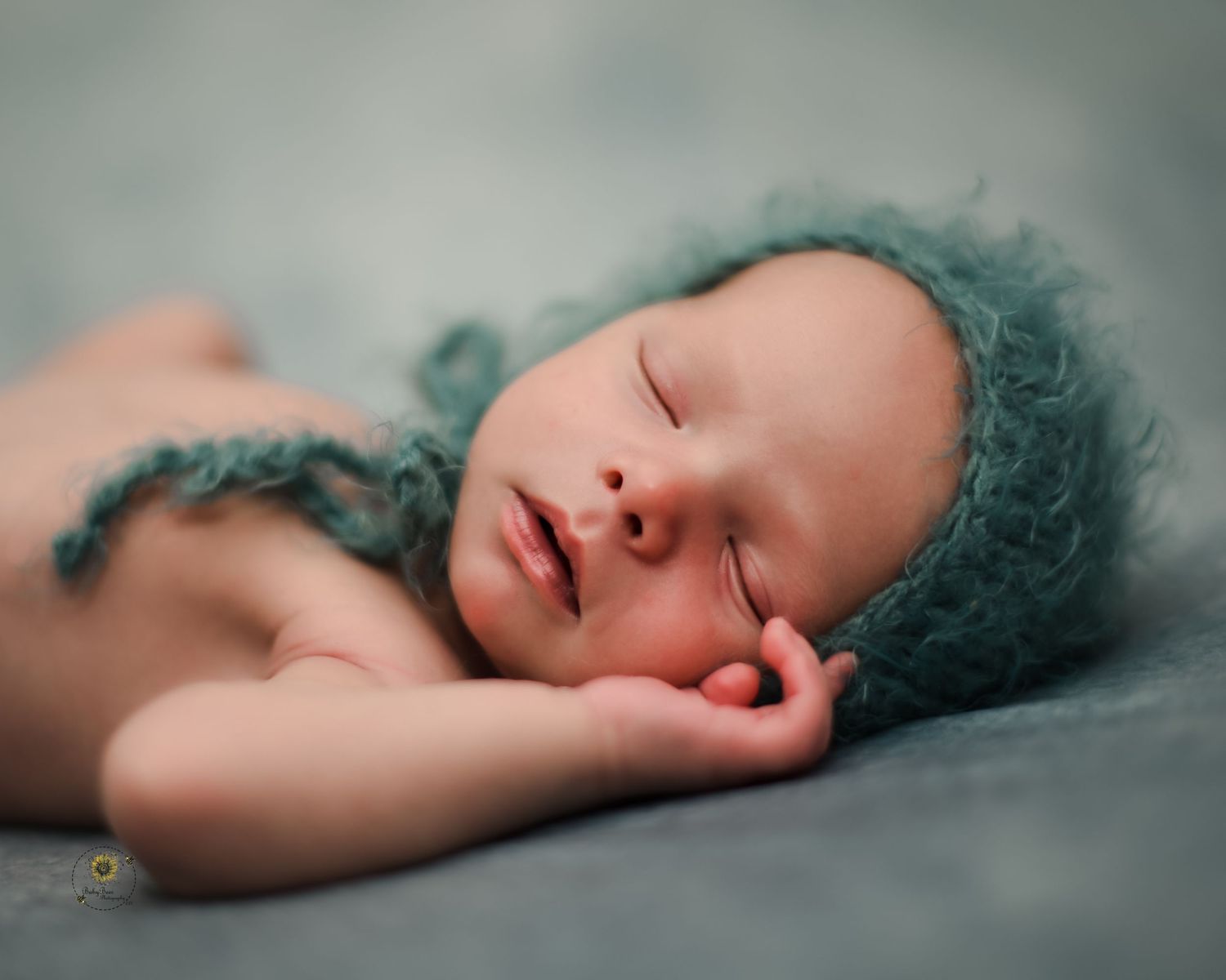 A peaceful sleeping baby rests on soft teal bedding in a dreamy artistic newborn portrait series.