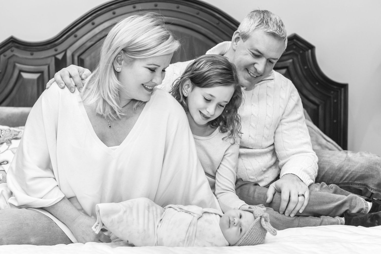 A family shares a tender moment together on a bed in black and white.