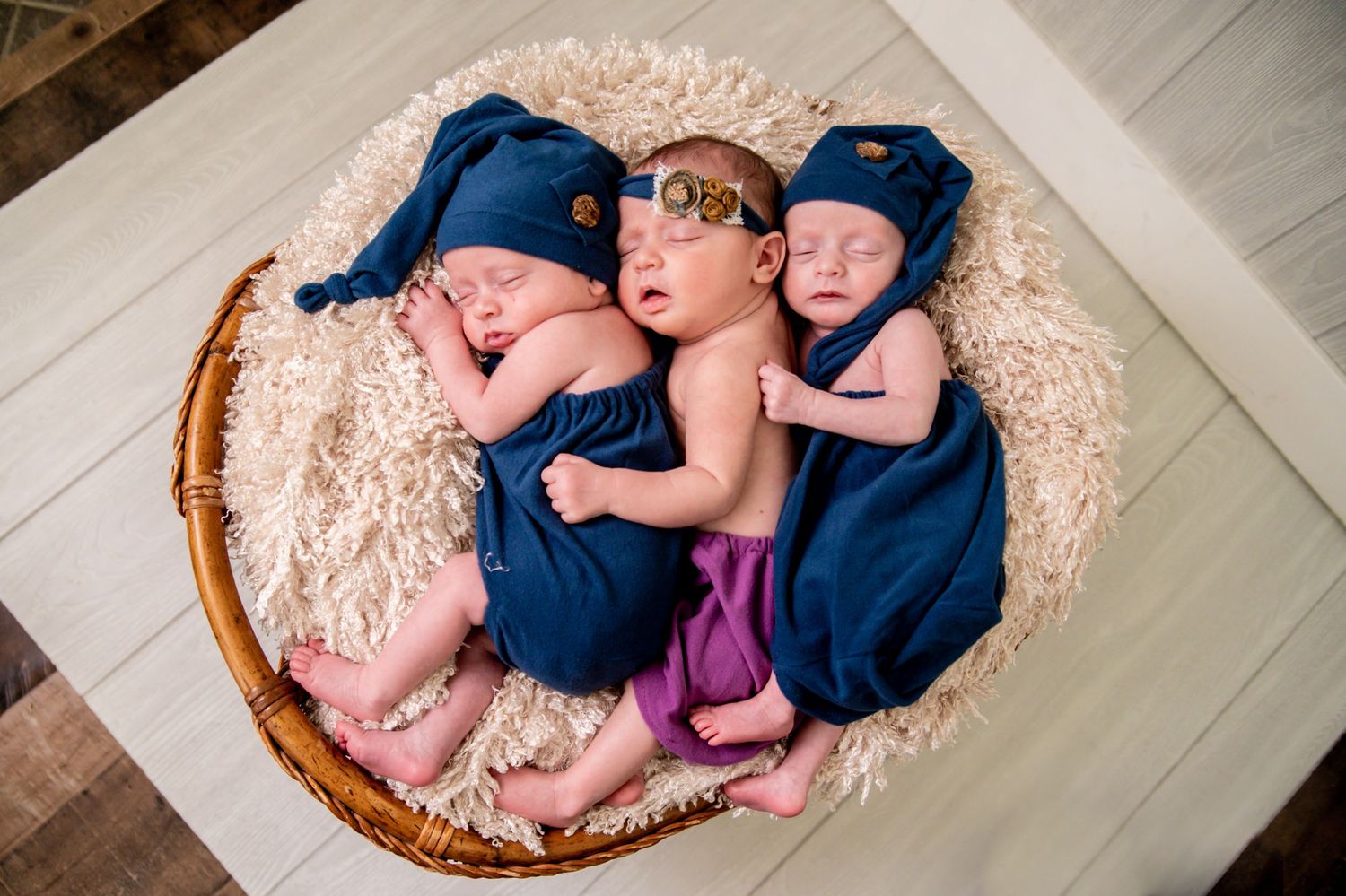 Newborn baby sleeping peacefully in a woven basket with pink and navy blue blankets.