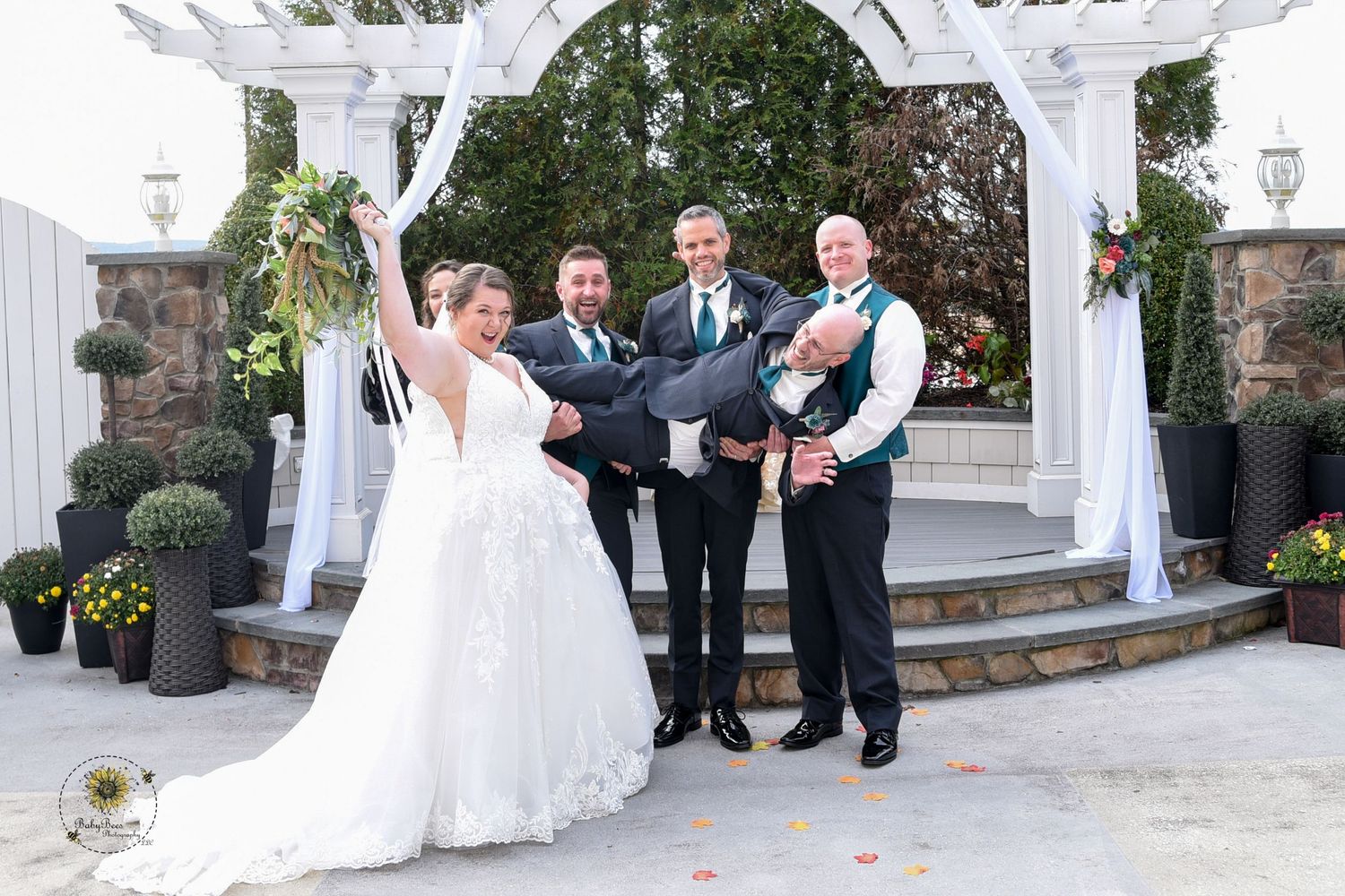 Wedding party poses under white pergola in outdoor garden setting.