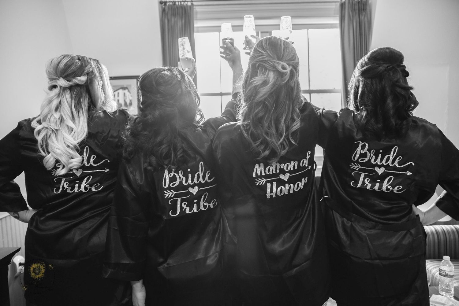 Row of matching black satin robes with white script text worn by bridal party.