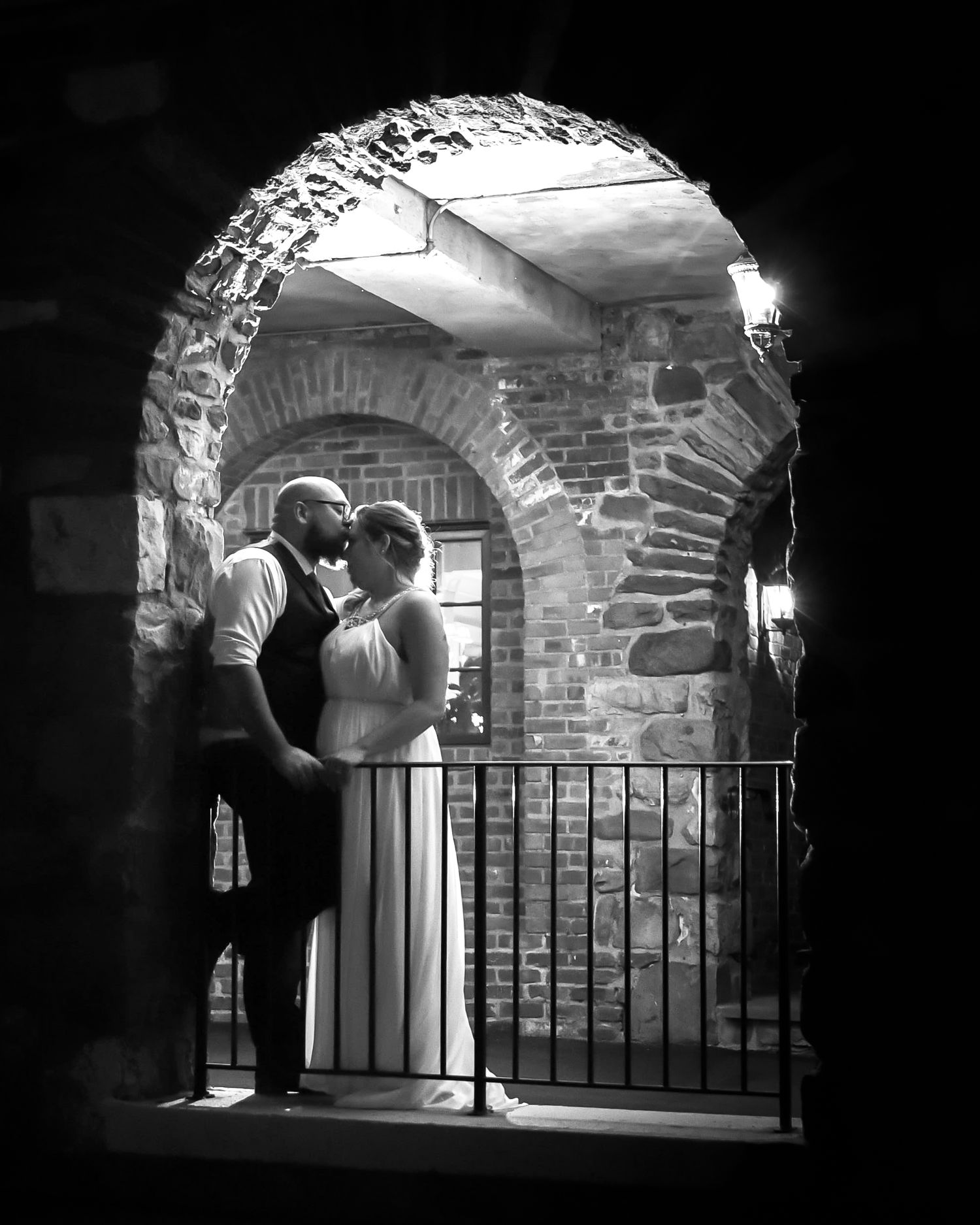 Black and white photo of romantic couple embracing in stone archway during wedding.