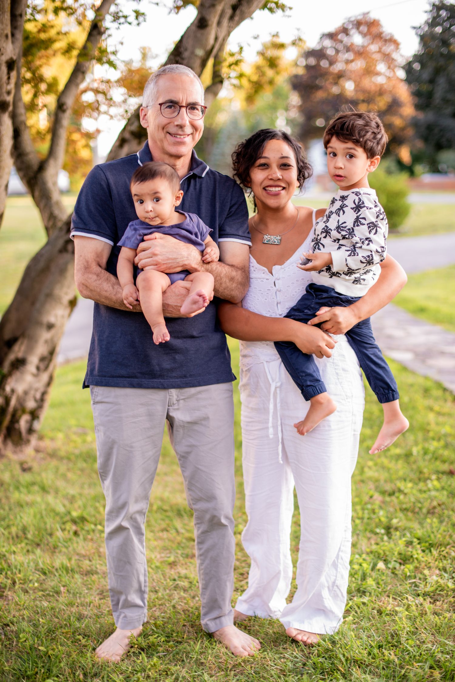 Family in coordinated navy and white outfits poses together outdoors during golden hour in autumn.
