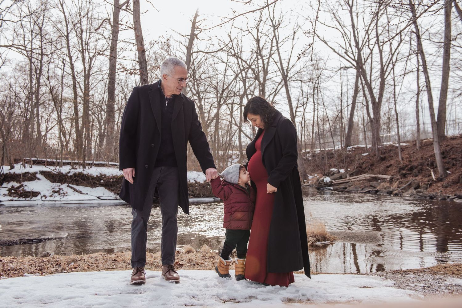 Two people walking together on a snowy winter path through bare trees in a forest setting.