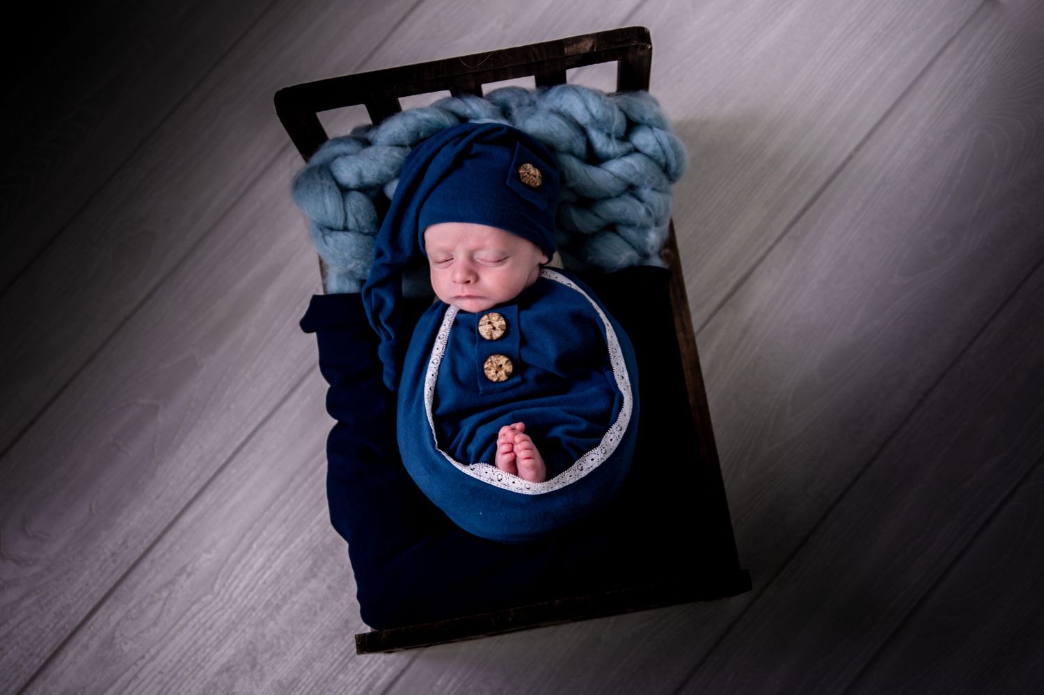 A newborn baby wrapped in a blue blanket sleeps peacefully in a series of black and white photographs.